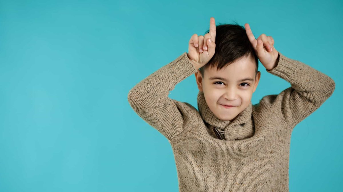 A little boy holds his fingers to his head posing as a bull.