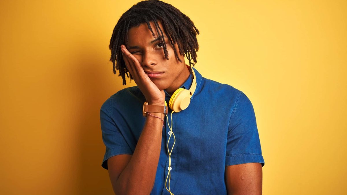 a young man wears headphones around his neck and holds his hand to his face as he leans into it with a sad, mournful look on his face as though the music he was listening to has made him melancholy, perhaps the blues.