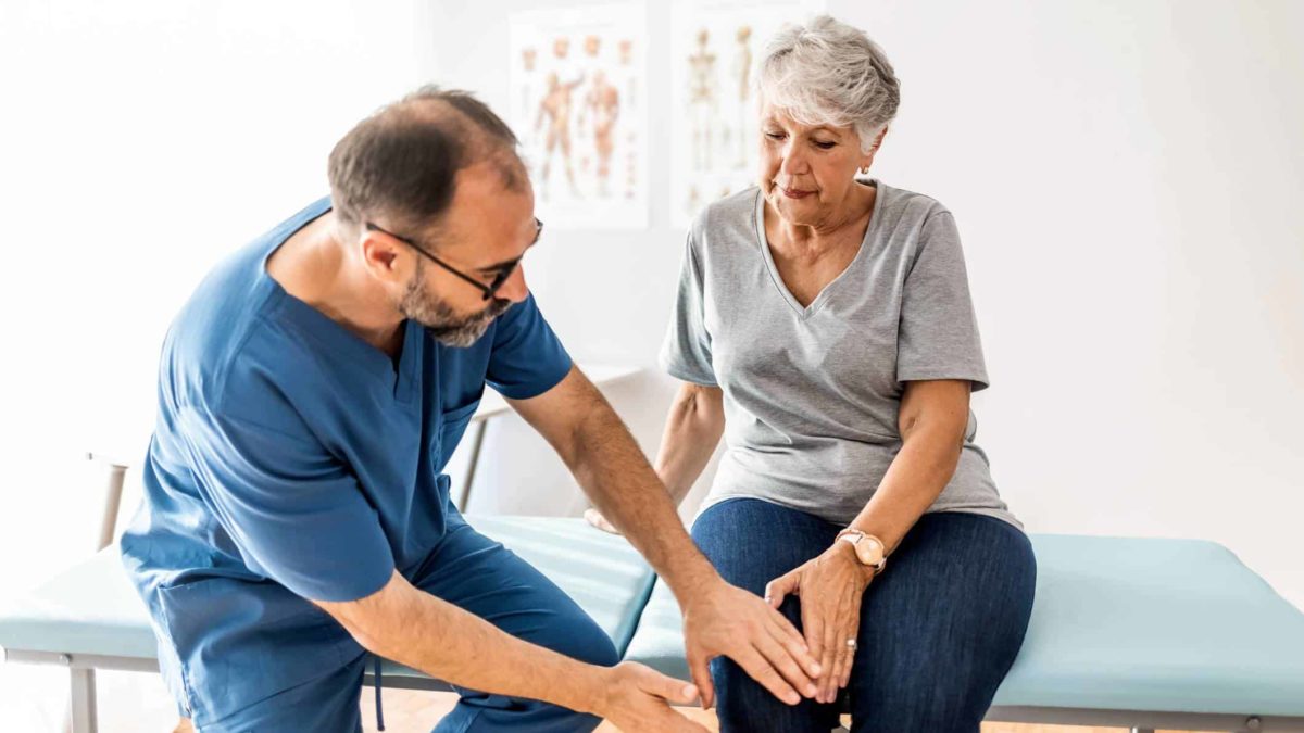 A woman sits on a doctor's table as he examines her knee for osteoarthritis as part of Paradigm's study