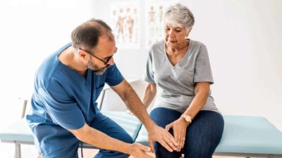 A woman sits on a doctor's table as he examines her knee for osteoarthritis as part of Paradigm's study