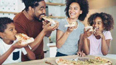 Two parents and two children happily eat pizza in their kitchen as a top broker predicts a 46% upside for the Domino's share price