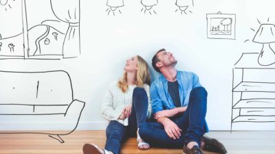 A couple sits on the floor with sketches of their dream home forming around them.