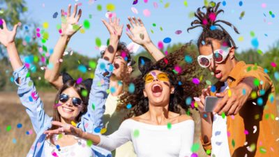 A group of friends party and dance in the desert with colourful confetti all around them.