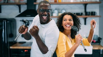 A man and woman dance back to back as they cook in kitchen.