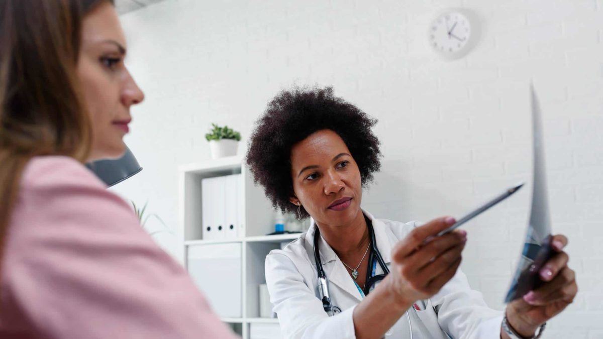 A doctor sits with a patient and uses a pen to point to certain parts of her mammogram scan