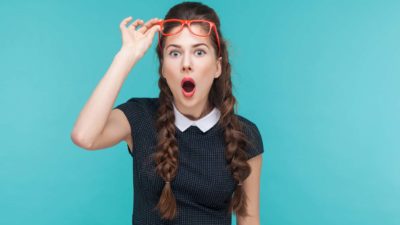 A young woman lifts her red glasses with one hand as she takes a closer look at news about interest rates rising and one expert's surprising recommendation as to which ASX shares to buy