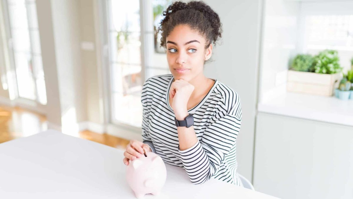 A woman looks questioning as she puts a coin into a piggy bank.