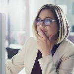 A woman sits at her computer with her hand to her mouth and a contemplative smile on her face as she reads about the performance of Allkem shares on her computer