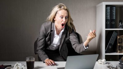 A businesswoman gets angry, shaking her fist at her computer.
