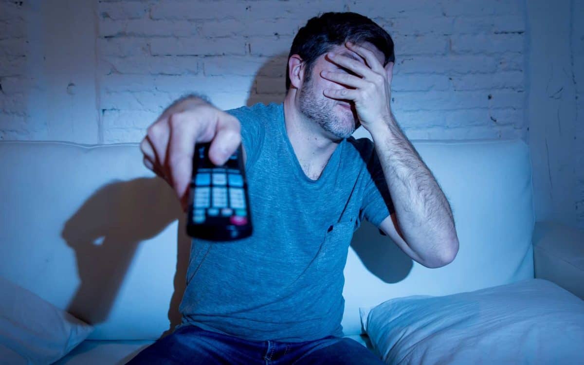 A man pointing a remote towards a TV whilst covering his eyes