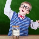 Young ASX share investor excitedly throwing hands up in front of savings jar.