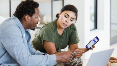 A couple sit in their home looking at a phone screen as if discussing a financial matter.
