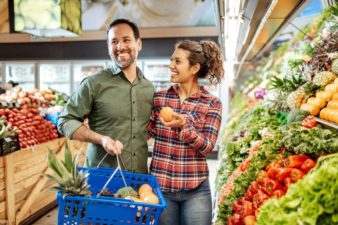 A couple in a supermarket laugh as they discuss which fruits and vegetables to buy